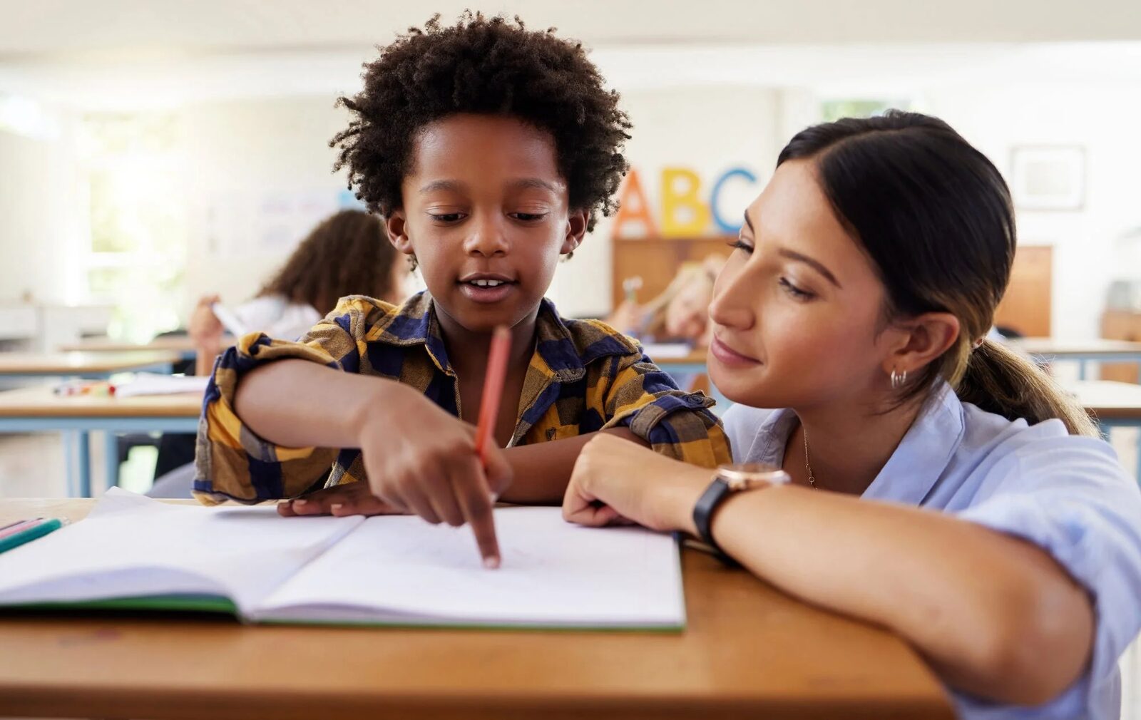 A school psychologist working with a student at a classroom desk